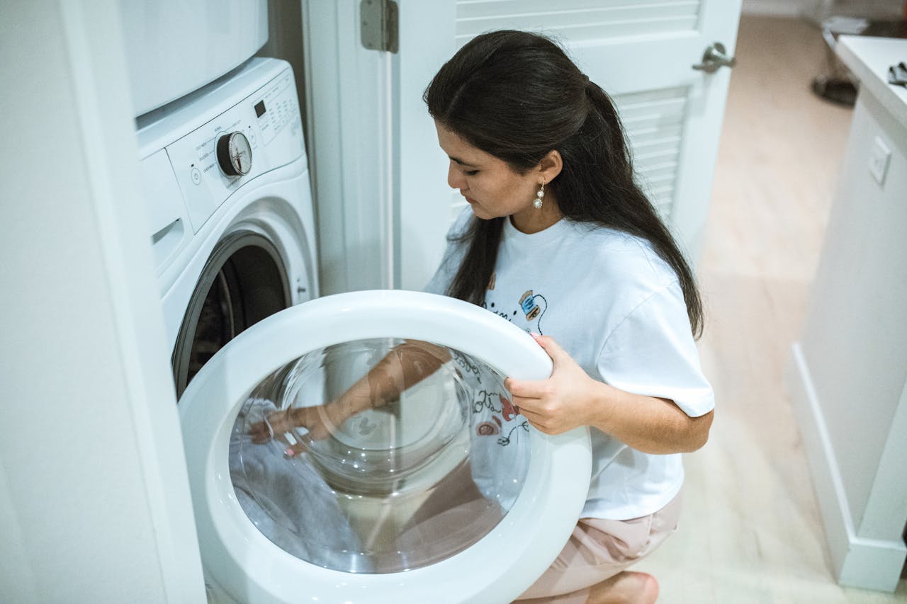 A woman kneeling to load clothes into a front-loading washing machine in a modern home laundry room.