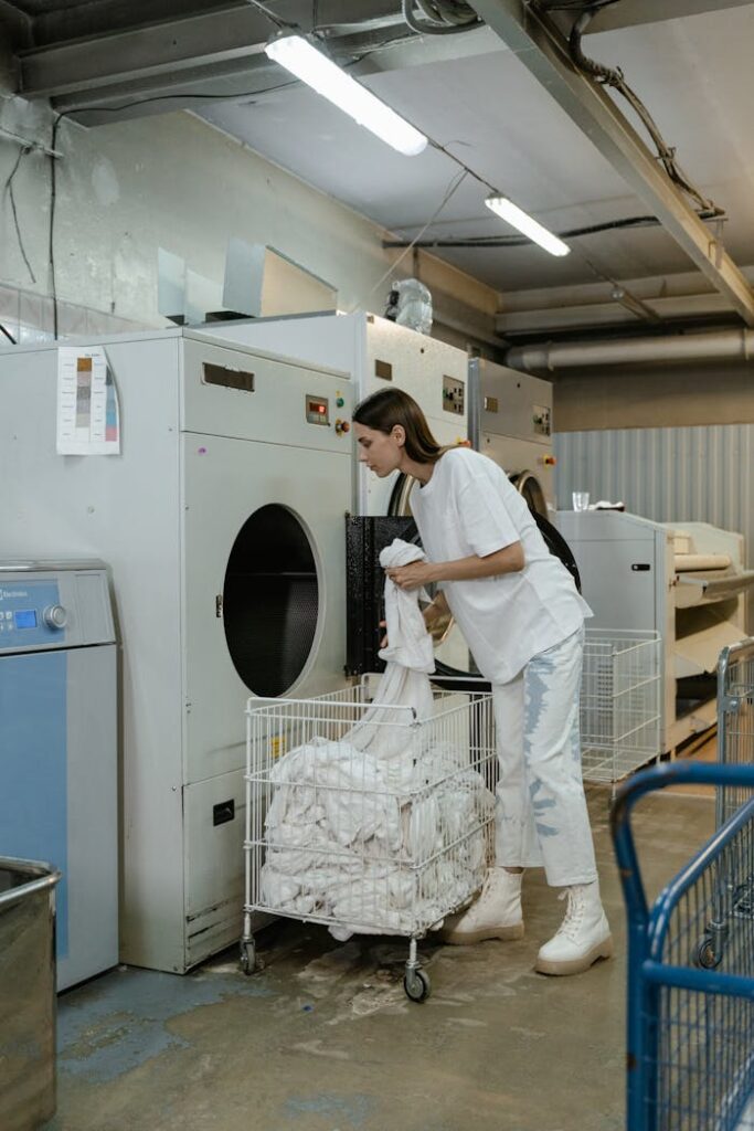 Woman working at a commercial laundry facility, operating a large washing machine with clothes.